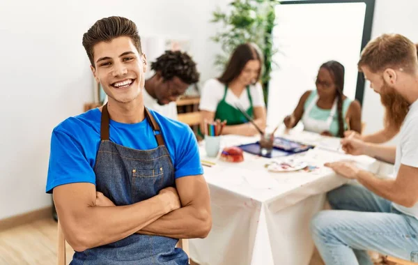 Group of people drawing sitting on the table. Hispainc man smiling happy looking to the camera at art studio.