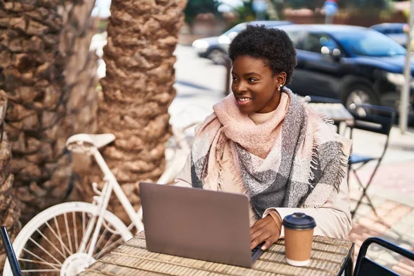 African american woman using laptop drinking coffee sitting on table at coffee shop terrace