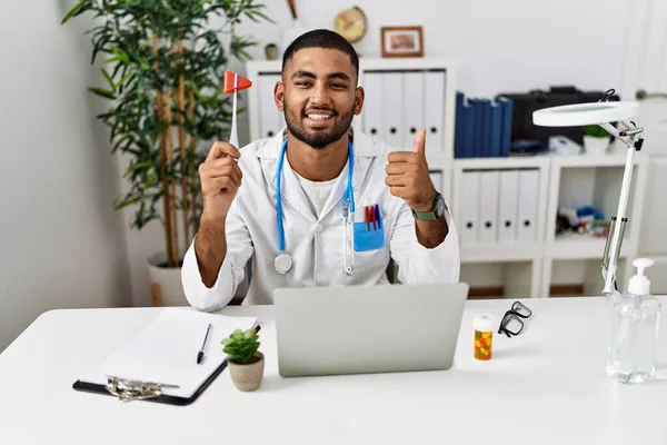 Young indian doctor holding reflex hammer smiling happy and positive, thumb up doing excellent and approval sign