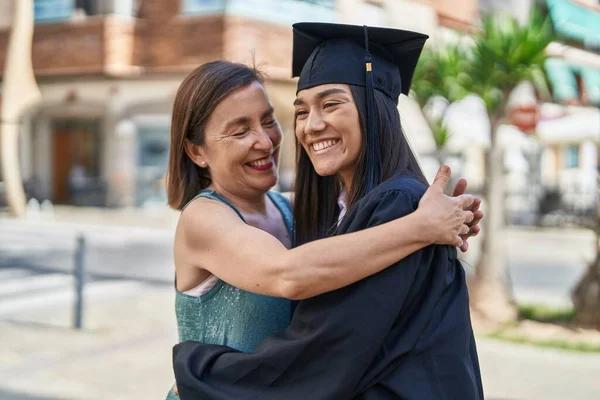 Two women mother and graduated daughter hugging each other at street