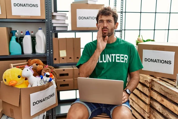 若いですハンサムな男を着てボランティアTシャツを使用してノートパソコンの手を口の中に秘密の噂を伝える ささやく悪意のある話会話 — ストック写真