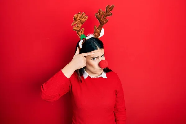 Young Hispanic Woman Wearing Deer Christmas Hat Red Nose Pointing — стоковое фото