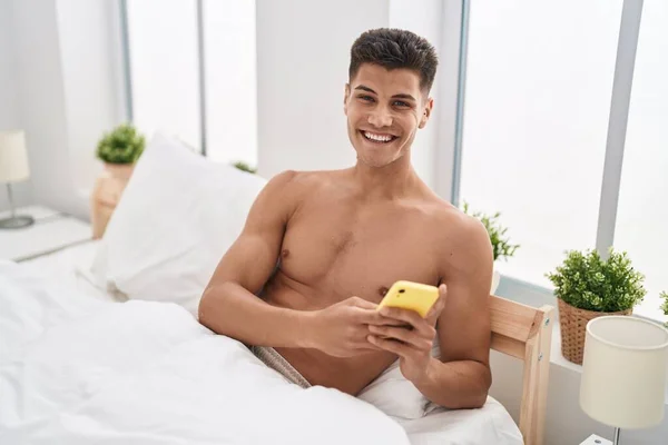 Young Hispanic Man Using Smartphone Sitting Bed Bedroom —  Fotos de Stock