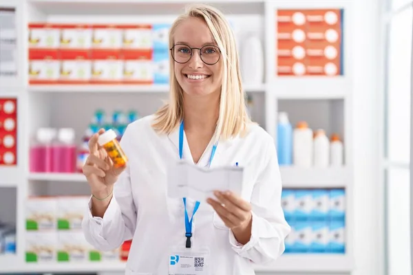 Giovane Donna Bionda Farmacista Possesso Pillole Bottiglia Lettura Prescrizione Farmacia — Foto Stock