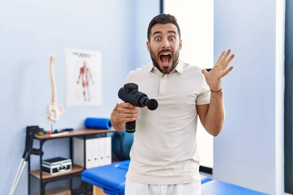 Schöner Hispanischer Mann Mit Therapie Massagepistole Physiotherapiezentrum Feiert Den Sieg — Stockfoto