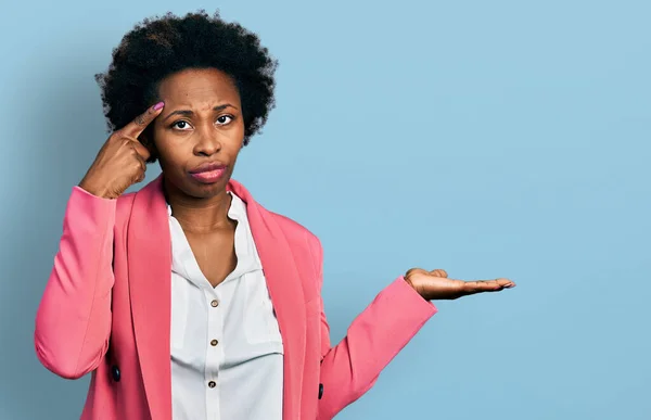 African american woman with afro hair wearing business jacket confused and annoyed with open palm showing copy space and pointing finger to forehead. think about it.