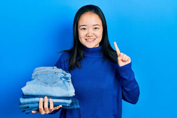 Young Chinese Girl Holding Stack Folded Jeans Smiling Idea Question — Stock Fotó