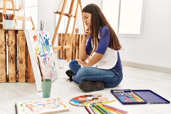 Resim stüdyosunda resim çizen şüpheyle bakan genç Latin kadın.