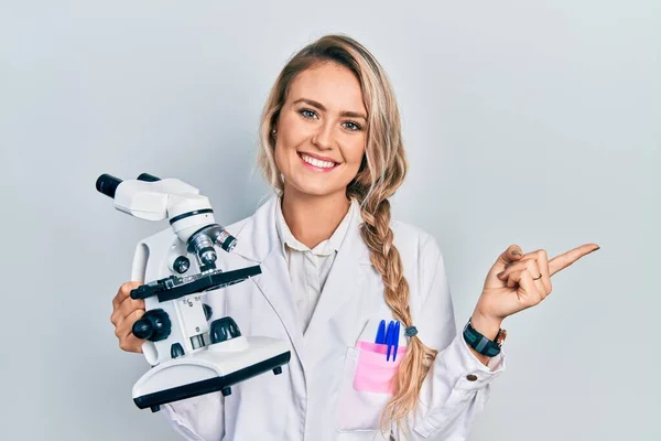 Beautiful Young Blonde Woman Holding Microscope Smiling Happy Pointing Hand —  Fotos de Stock
