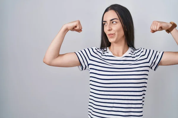 Young Brunette Woman Wearing Striped Shirt Showing Arms Muscles Smiling — Stockfoto