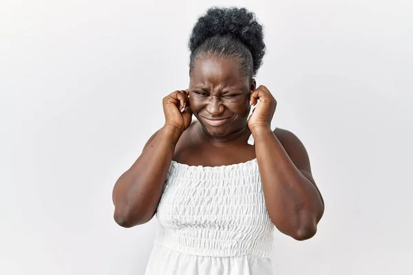 白い孤立した背景の上に立つ若いアフリカ人女性は 大きな音楽のノイズに悩まされた表情で指で耳を覆います 聴覚障害の概念 — ストック写真