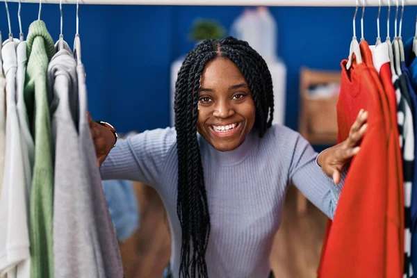 African american woman searching clothes on clothing rack smiling and laughing hard out loud because funny crazy joke.
