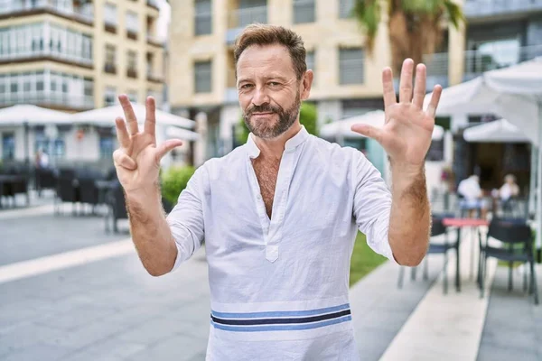 Middle age man outdoor at the city showing and pointing up with fingers number nine while smiling confident and happy.