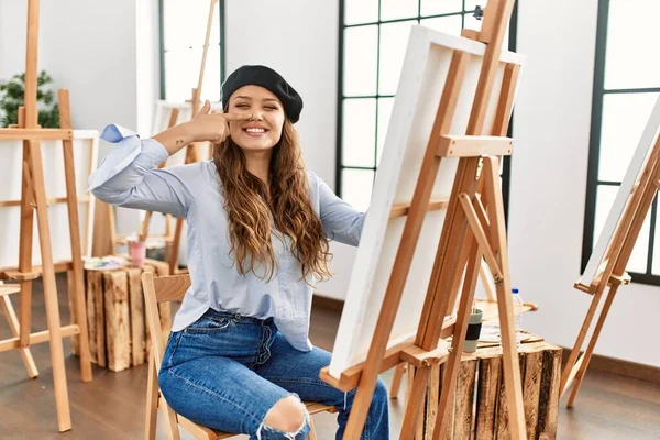 若いヒスパニック系のアーティストの女性が顔や鼻に手指で指してアートスタジオでキャンバス上で絵を描く 陽気に笑顔 美の概念 — ストック写真