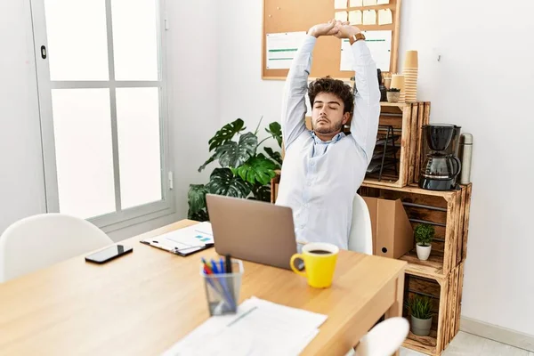Young hispanic businessman relaxed stretching arms at the office.