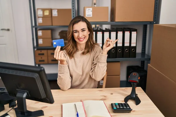 Young woman working at small business ecommerce holding credit card smiling happy pointing with hand and finger to the side