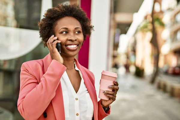 Beautiful business african american woman with afro hair smiling happy and confident outdoors at the city having a conversation speaking on the phone