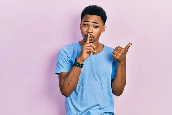 若いアフリカ系アメリカ人の男性は カジュアルなブルーのTシャツを着て 唇に手で側に指して指で静かになるように求めています 沈黙と秘密の概念 — ストック写真