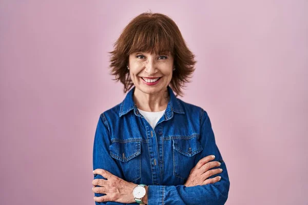 Middle age woman standing over pink background happy face smiling with crossed arms looking at the camera. positive person.