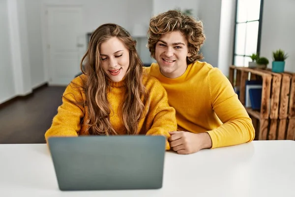年轻的高加索夫妇带着自信的笑容在家里使用笔记本电脑 — 图库照片