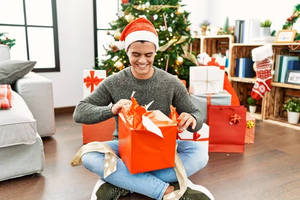 Jovem Hispânico Desempacotando Presente Sentado Árvore Natal Casa — Fotografia de Stock