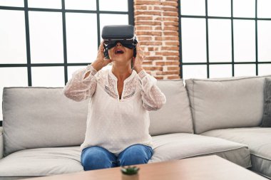 Evde sanal gerçeklik gözlüğü kullanan orta yaşlı bir kadın video oyunu oynuyor.
