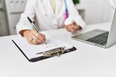 Orta yaşlı İspanyol kadın klinikte elinde haplarla doktor üniforması giyiyor.