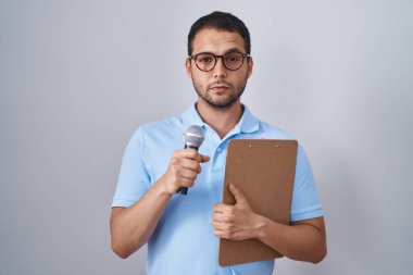 Hispanic man holding reporter microphone and clipboard depressed and worry for distress, crying angry and afraid. sad expression. 