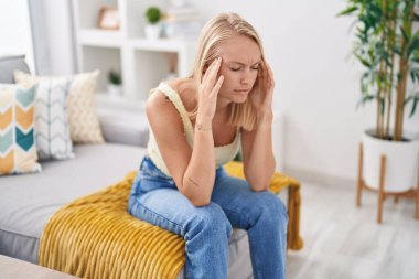 Evdeki kanepede oturan genç sarışın kadın baş ağrısı çekiyor.