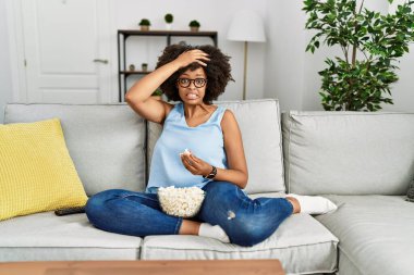 Afro saçlı Afro-Amerikan bir kadın evde patlamış mısır yiyor. Stresli ve hayal kırıklığına uğramış, şaşırmış ve kızgın bir yüzü var. 