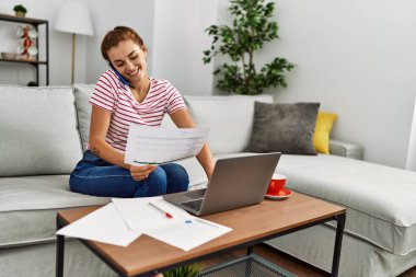 Akıllı telefondan konuşan ve evde çalışan genç bir kadın.