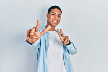 Gündelik giysiler giymiş genç Afro-Amerikan adam kameraya bakıp zafer işareti yapıyor. İki numara.. 