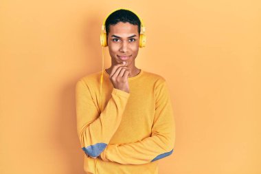 Genç Afro-Amerikalı adam müzik dinliyor kulaklık takıyor kameraya bakıyor kollarını kavuşturup gülümsüyor ve çenesini kaldırıyor. Olumlu düşünmek. 