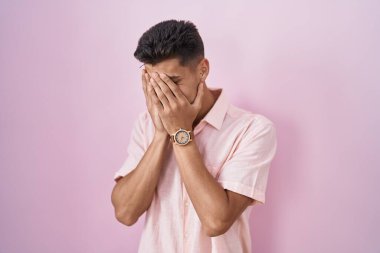 Pembe arka planda duran genç İspanyol bir adam. Ağlarken suratını ellerle kapatan üzgün bir ifade. depresyon kavramı. 