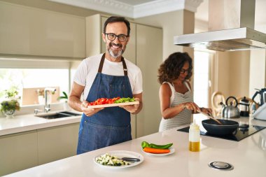 Orta yaşlı bir çift evde Akdeniz yemeği pişiriyor mutlu ve serin bir gülümsemeyle gülümsüyor. diş gösterme. 