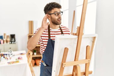 Sanat stüdyosunda ağzı kulaklarında gülümseyen Arap genç bir adam dedikoduları ve dedikoduları dinliyor. Sağırlık kavramı. 