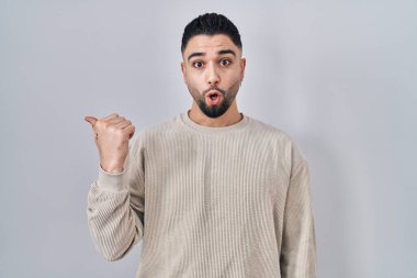 İzole edilmiş arka planda duran yakışıklı genç adam, elleri yana doğru işaret ederek şaşırdı, ağzı açık hayret içinde kaldı.. 