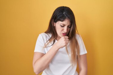 Sarı arka planda duran esmer kadın kendini iyi hissetmiyor ve soğuk algınlığı veya bronşitin belirtisi olarak öksürüyor. sağlık hizmeti kavramı. 