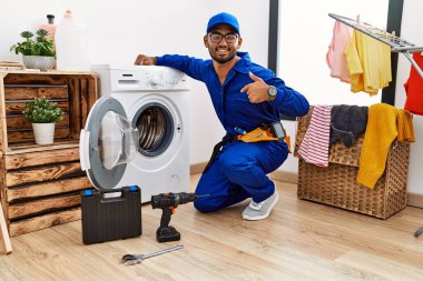 Young indian technician working on washing machine looking confident with smile on face, pointing oneself with fingers proud and happy. 