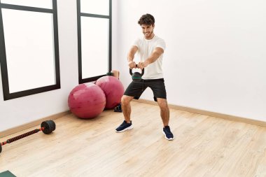 Young hispanic man smiling confident training with kettlebell at sport center