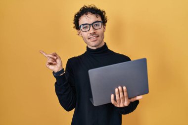 Hispanic man working using computer laptop smiling happy pointing with hand and finger to the side 