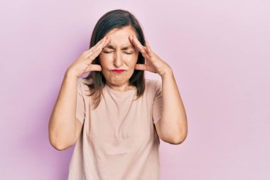 Orta yaşlı İspanyol kadın stres yüzünden elleri başının üstünde gündelik kıyafetler giyiyor. migren ağrısı. 