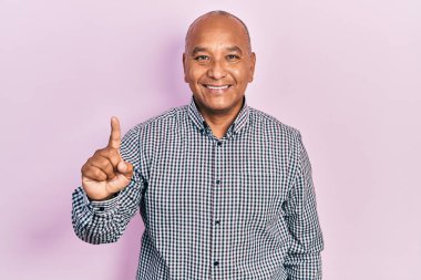 Orta yaşlı, gündelik kıyafetler giyen Latin bir numaralı parmağını gösterip işaret ederken kendinden emin ve mutlu bir şekilde gülümsüyor.. 