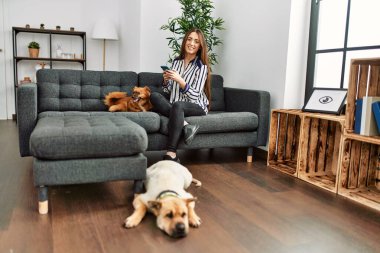 Genç İspanyol kadın akıllı telefon kullanıyor. Kanepede köpeklerle oturuyor.
