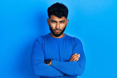 Arab man with beard wearing casual blue sweater skeptic and nervous, disapproving expression on face with crossed arms. negative person. 