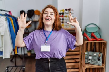 Perakende mağazasında yönetici olarak çalışan genç kızıl saçlı kadın dokuz numarayı gösterip işaret ederken kendinden emin ve mutlu bir şekilde gülümsüyor.. 