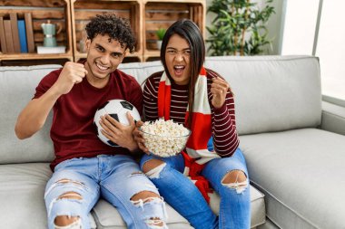 Evdeki kanepede oturan genç latin çift futbol maçını izliyor ve destekliyor..