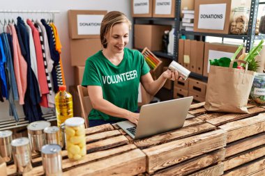 Young caucasian woman wearing volunteer uniform holding canned food working at charity center