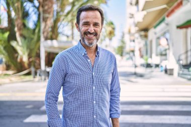 Orta yaşlı İspanyol gülen adam şehirde mutlu bir şekilde duruyor..