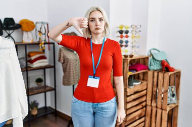 Young caucasian woman working as manager at retail boutique looking unhappy and angry showing rejection and negative with thumbs down gesture. bad expression. 